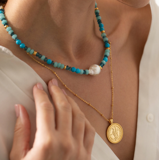 Gemstone beaded necklace featuring Aventurine and Turqouise beads, a large central Baroque freshwater pearl in the middle, and small 18k gold plated beads spaced out throughout the gemstones. Worn on a model wearing a ZARA white shirt with the buttons undone and another Gold Lunar 18k gold plated necklace with a coin pendant.