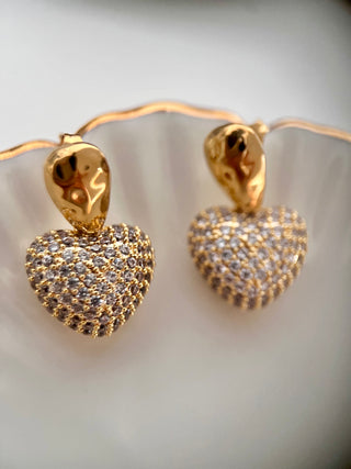 Cubic Zirconia encrusted heart drops on a hammered 18k gold plated earring displayed on a white jewellery dish