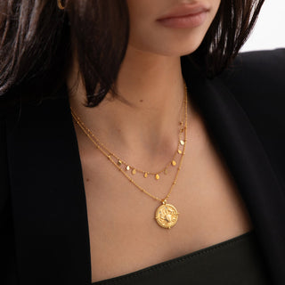 18k gold plated brass Cancer star sign Zodiac Necklace with cubic zirconia stones and intricate detailing on a coin disc pendant and on fine ball chain worn on a model with a dainty fine chain layering necklace and wearing a black Zara blazer.