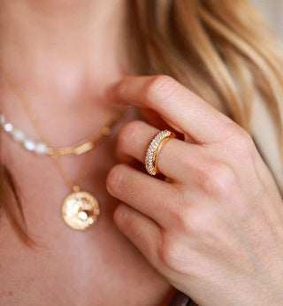 gold plated band ring with Cubic Zirconia  stones around the centre worn by a model wearing a zodiac necklace and a pearl and ink chain necklace 