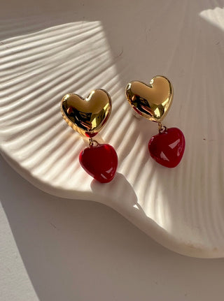 Gold heart earrings with red heart drops displayed on a white pretty jewellery dish with the sun shining in