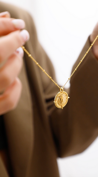 18k gold plated brass Taurus Zodiac Necklace with cubic zirconia stones and intricate detailing on a coin disc pendant and on fine ball chain about to be put on a model wearing a brown Zara blazer.