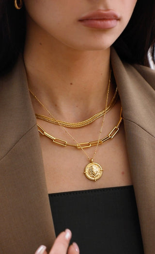 18k gold plated brass Taurus Zodiac Necklace with cubic zirconia stones and intricate detailing on a coin disc pendant and on fine ball chain - worn on a model wearing a black top and brown blazer from Zara and layered with a chunky link chain and a slinky woven chain.