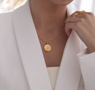 18k gold plated brass Taurus Zodiac Necklace with cubic zirconia stones and intricate detailing on a coin disc pendant and on fine ball chain - worn on a model wearing white blazer from Zara and multiple gold rings from Gold Lunar