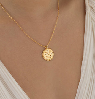 18k gold plated brass sagittarius  Necklace with cubic zirconia stones and intricate detailing on a coin disc pendant and on fine ball chain - worn by a model wearing a cream pleated blouse from Zara