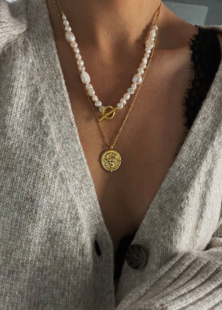 18k gold plated brass Taurus Zodiac Necklace with cubic zirconia stones and intricate detailing on a coin disc pendant and on fine ball chain - worn on a model wearing a black lace bra and a grey knitted cardigan and layered with freshwater pearl necklace