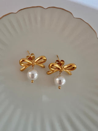 18k gold plated pretty bow earrings with a faux pearl drop displayed on a white jewellery dish with gold edge