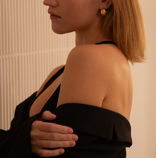 18k gold plated chunky hoops with etched design worn on a model wearing a black top and blazer off the shoulder