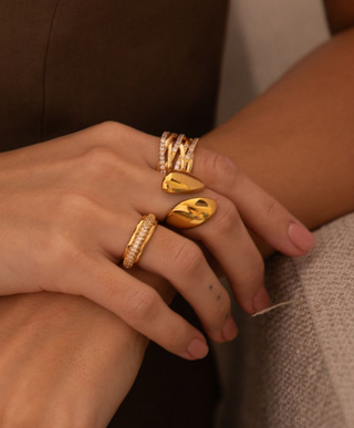 18k gold plated rings worn across fingers with the Chunky Wrap Ring, cubic zirconia wrap crossover ring and the cubic zirconia halo band ring worn on a model wearing a brown Zara waistcoat