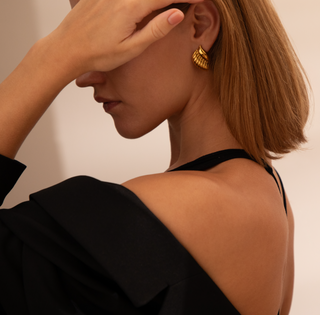 18k gold plated curve studs with ribbed detail worn on a model wearing a black top and blazer worn off the shoulder