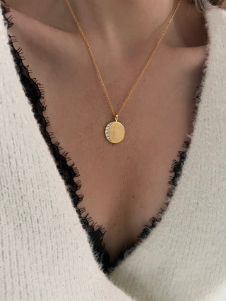 18k gold plated celestial moon disc with Cubic Zirconia stones in a crescent moon shape on a hammered molten disc on fine chain necklace worn on a model wearing a black lace brand wn white fluffy jumper