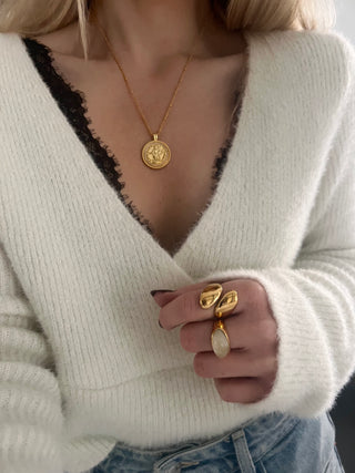 18k gold plated coin pendant necklace with cubic zirconia gemstones around the outside on a fine gold chain worn on a model wearing a black lace bra, white fluffy v neck jumper and denim wide leg jeans. also wearing two chunky 18k gold plated rings, one with a new jade gemstone.