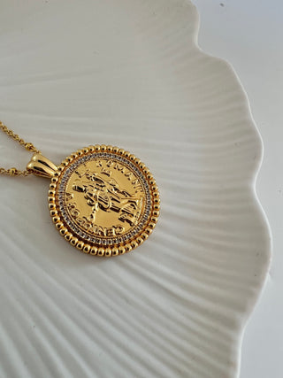 18k gold plated coin pendant necklace with cubic zirconia gemstones around the outside on a fine gold chain displayed on a pretty white porcelain jewellery dish