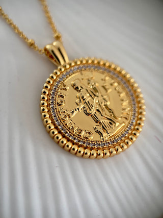 18k gold plated coin pendant necklace with cubic zirconia gemstones around the outside on a fine gold chain displayed on a pretty white jewellery dish close up