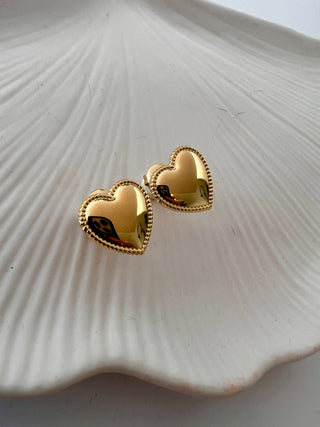 puffy heart studs earrings in gold with intricate detailing around the edge displayed on a pretty white jewellery dish