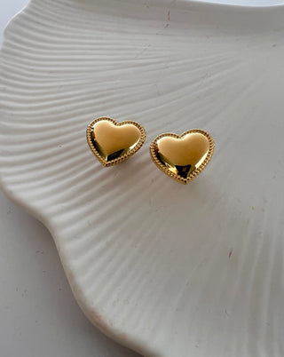 Puffy heart stud earrings with intricate detailing around the edge displayed on w white jewellery dish