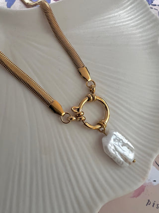 gold plated herringbone chain with a large round clasp and a large freshwater rectangular shaped pearl chain on a white dish