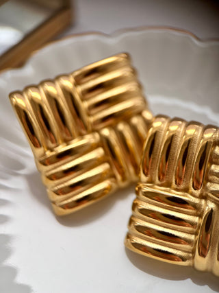 Large 18k gold plated stud earrings with criss cross detail displayed on a white jewellery dish close up