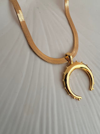 18k gold plated crescent moon pendant on a fine snake chain displayed on a white ceramic plate