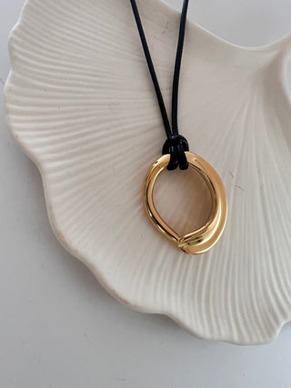 18k gold plated organic shaped round pendant on a cord black faux leather fabric displayed on a white pretty jewellery dish