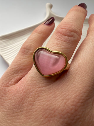 pink cats eye puffy heart ring in gold worn on a model hand with burgundy long pointed nails