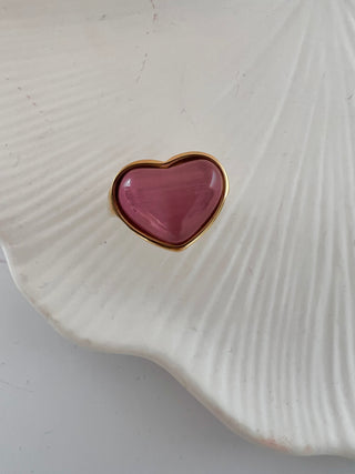 pink cats eye puffy heart ring in gold displayed on a white jewellery dish