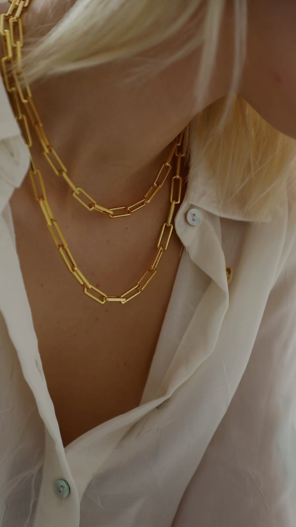 18k Gold plated brass Paperclip Chains worn by model wearing a ZARA semi sheer shite shirt with the buttons undone. model has blond hair and multiple gold rings worn across fingers.