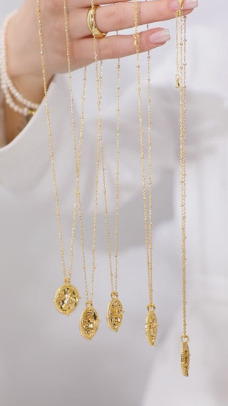 zodiac necklaces collection hanging from model's hand wearing a pearl bracelet and  gold ring.