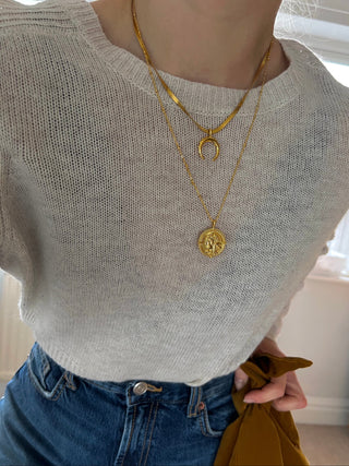 gold snake chain with crescent moon pendant with a longer necklace on fine ball chain with a coin pendant worn by model wearing a cream knit jumper from Zara and blue high waist wide jeans from Zara. holding a brown bag from makeup beauty brand Merit.